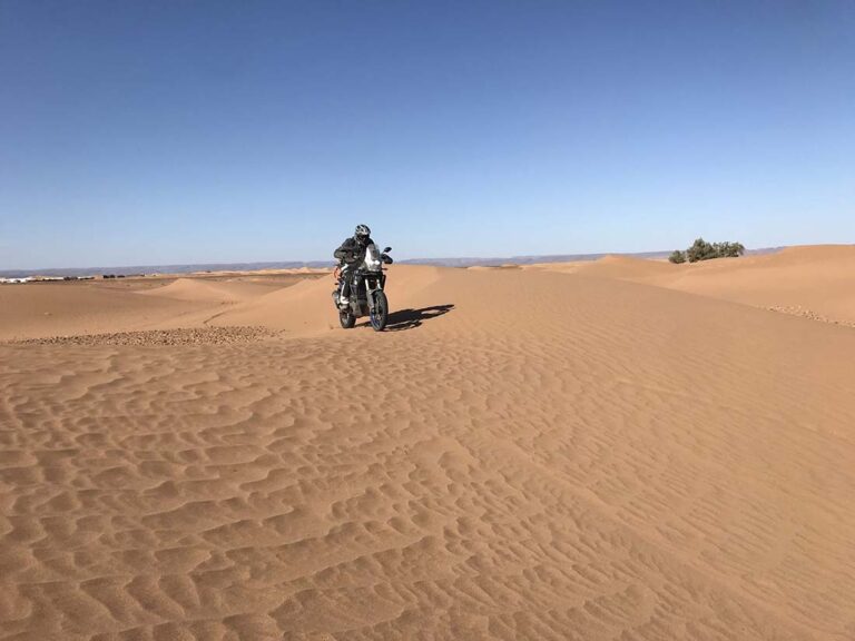 Pilote sur sa moto dans les dunes du Sahara marocain, un terrain qui demande un équipement renforcé