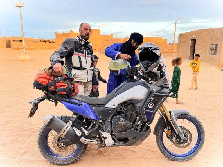 Pilote équipé d'une veste et d'un pantalon de protection à côté de sa Yamaha Ténéré 700 dans un village du sud marocain
