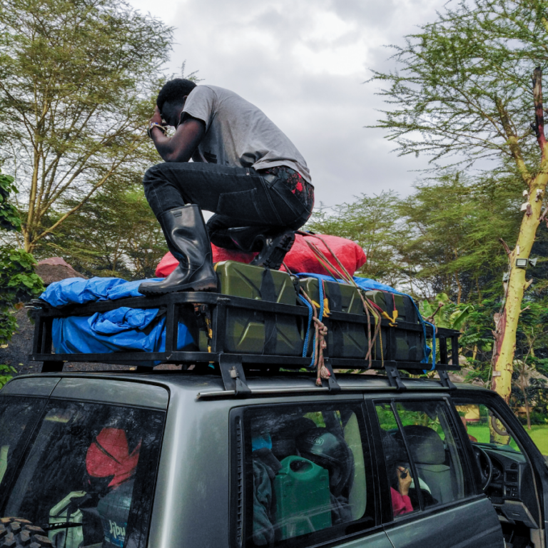 Membre de l'équipe locale chargeant les bagages sur le toit du 4x4 d'assistance en Tanzanie