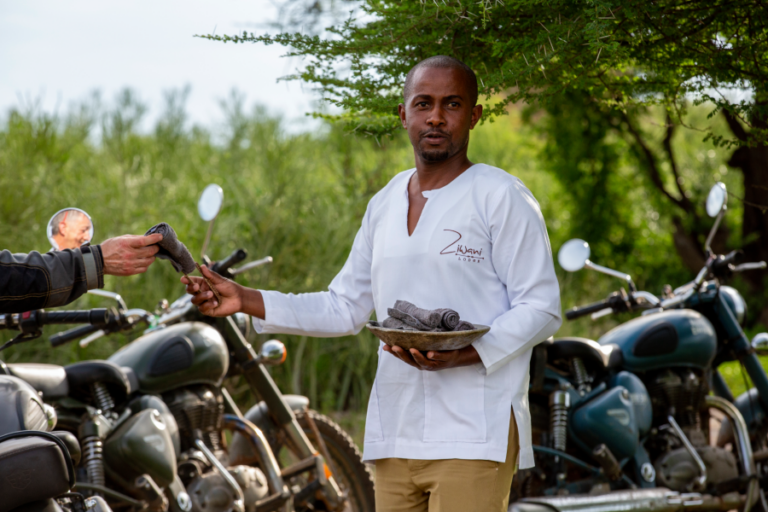 Membre de l'équipe locale servant des boissons aux voyageurs à côté des motos en Tanzanie