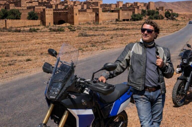 Voyageur souriant à côté de sa Yamaha Ténéré 700 devant une kasbah au Maroc, une moto pour un road trip sur les pistes de l'Atlas